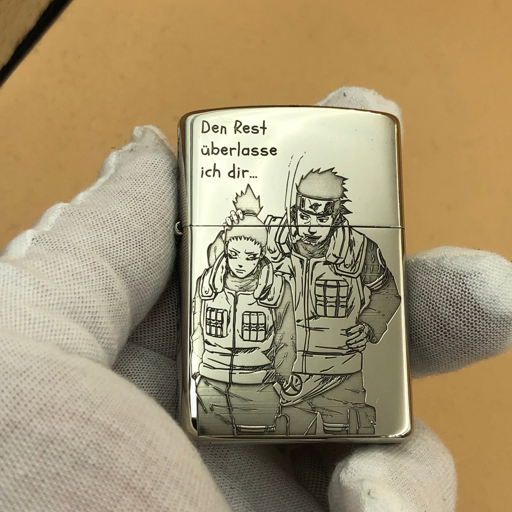 Silver lighter with engraved design held by a gloved hand against a beige background
